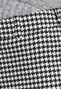 Black and white houndstooth patterned fabric with a textured finish, featuring a distinctive alternating design and visible stitching details.