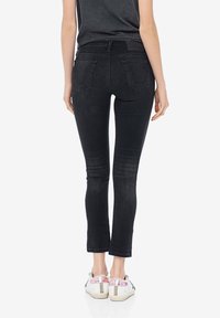 Jeans skinny in denim nero con vita alta, tasche posteriori e leggero sbiadimento, abbinati a sneakers bianche con dettagli rosa.