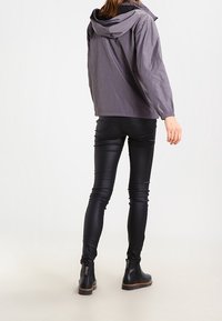 Šedá kapucínová bunda s elastickými manžetami, spárovaná s černými koženými legínami a kotníkovými botami, ukazující elegantní střih a zúžený design.