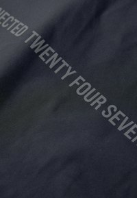 Tissu sombre avec un texte partiellement gris clair indiquant "VINGT QUATRE SEPT" en lettres majuscules et en gras.