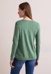 Pull vert à manches longues avec un col rond, tricot texturé et bords côtelés. Porté avec un jean bleu, montrant une silhouette ajustée de dos.