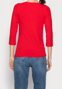 Rotes Langarm-T-Shirt aus leichtem Stoff, mit rundem Halsausschnitt und taillierter Passform, kombiniert mit hochgeschnittenen Jeans.