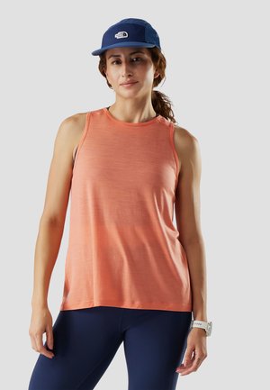 Kvinde iført en koralfarvet ærmeløs top, mørkeblå leggings, hvidt armbåndsur og blå kasket med The North Face-logo, stående mod en ensfarvet baggrund.