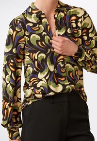 Blusa con motivo caratterizzata da uno sfondo nero e da affascinanti disegni colorati in verde, blu, arancio e crema; stile a bottoni con maniche lunghe.
