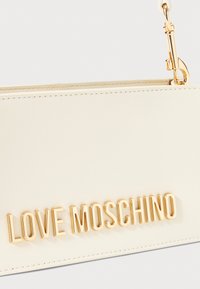 Kreemi nahast üleõla kott tekstuuriga viimistlusega, millel on kuldse tooni "LOVE MOSCHINO" logo ja kuldne metallist aksessuaaride viimistlus.