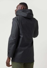 Chaqueta impermeable negra con capucha, con una textura lisa, mangas largas y puños ajustables. La vista trasera muestra un diseño sencillo.