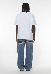White cotton t-shirt with short sleeves, paired with distressed wide-leg blue jeans featuring frayed edges and patch detailing.