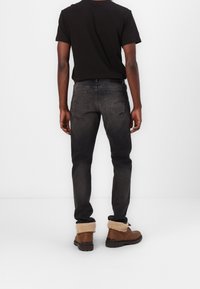 Vaqueros de denim negro con un corte ajustado, textura desgastada, cinco bolsillos y una cintura de altura media, combinados con botas marrones con forro de piel.