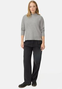 Pull en tricot gris avec capuche, manches longues et texture côtelée. Associé à un pantalon en denim noir à jambes larges et des sabots noirs.