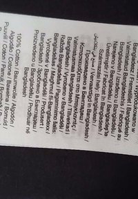 Etiketti, jossa on moniväristä tekstiä valkoisessa kangasmerkissä, jossa lukee "100 % puuvillaa" useilla eri kielillä ja mainitaan alkuperäksi Bangladesh.