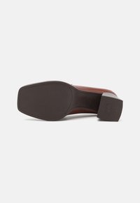 Suela de zapato de cuero marrón mirando hacia arriba, tacón cuadrado con texto "Antideslizante", superficie texturizada en la suela y el tacón, aislado sobre fondo blanco.