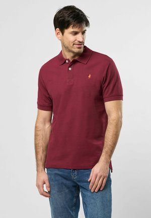 Camisa polo burdeos con cuello y mangas cortas. Presenta un pequeño logo bordado y una tela texturizada. Combinada con unos vaqueros azules.