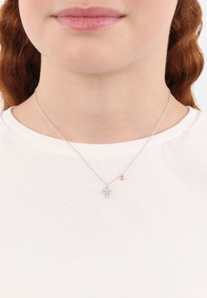 Collana d'argento con un piccolo ciondolo dal design dettagliato e un accento decorativo in oro rosa. Indossata sopra una maglietta bianca.