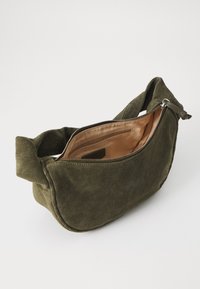 Borsa in suede verde oliva con forma curvata, chiusura con zip e interno morbido. Presenta una tracolla larga e cuciture minime come dettaglio.