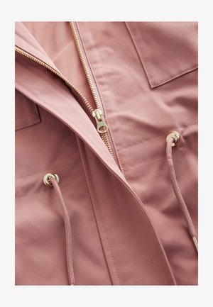 Heledad roosa jakk, millel on kuldne lukk, reguleeritavad nöörid ja kaks rinna-taskut, valmistatud siledast kangast, millel on veidi matt tekstuur.