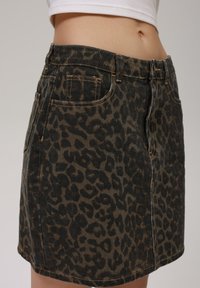 Denimskjørt i brun og svart leopardmønster. Har femlommersdesign, beltehemper og en litt slitt hem.