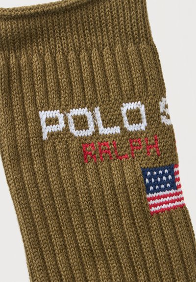 Καφέ πλεκτό ύφασμα με λευκό κείμενο "POLO S," κόκκινο κείμενο "RALPH," και μια μικρή κεντημένη αμερικανική σημαία.