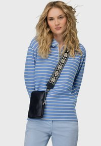 Pasiasta niebiesko-biała koszulka polo z zamkiem, noszona z jasnoniebieskimi spodniami. Czarna teksturowana torba na ramię z haftowanym paskiem.