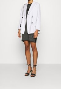 Blazer à double boutonnage lavande clair avec des boutons noirs, associé à une robe noire texturée ajustée et des sandales noires à talons avec brides.