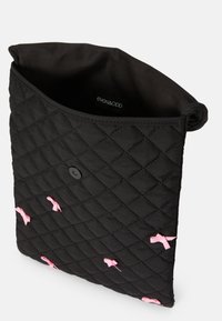 Geantă neagră matlasată cu accente din panglică roz, închidere cu clapetă și căptușeală moale; formă rectangulară compactă cu suprafață texturată.