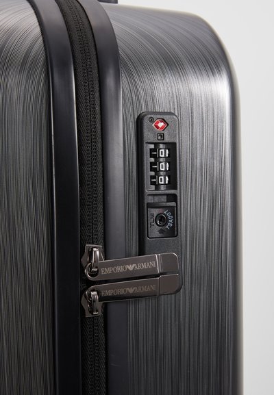 Maleta rígida negra con superficie texturizada, tiradores de doble cremallera con marca, cerradura de combinación y detalles de hardware en color contrastante.