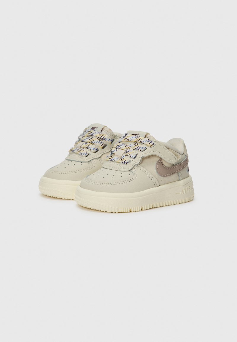 Jasno-beżowe sneakersy z teksturowaną skórzaną cholewką, kontrastowym szarym logo, perforowanym przodem oraz wielokolorowymi plecionymi sznurówkami. Guma podeszwy.