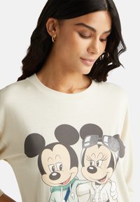 Krémová mikina s potiskem dvou kreslených myší s výraznými rysy obličeje a třpytivým akcentem na slunečních brýlích jedné myši.