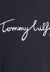 Marineblauwe sweatshirt met een opvallend wit geborduurd "Tommy Hilfiger"-logo in cursief lettertype over de voorkant. Gladde textuur.