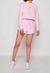 Completo da lounge rosa composto da un top cropped con maniche lunghe e pantaloni corti, realizzato in tessuto morbido. I pantaloni corti hanno una vita regolabile con coulisse.