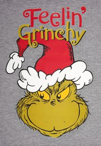 Tessuto grigio con una grande illustrazione del volto del Grinch, giallo-verde con baffi e berretto da Babbo Natale rosso. Il testo recita "Mi sento Grinchy" in rosso e giallo.