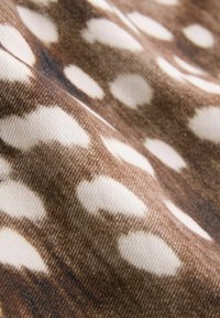 Tissu marron avec des taches ovales blanches irrégulières, texturé et légèrement froissé, ressemblant à un motif d'imprimé animal.