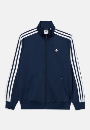 Granatowa kurtka sportowa na zamek błyskawiczny z białymi trzema paskami na rękawach, dwoma kieszeniami z zamkiem z przodu i małym, białym logo Adidas na piersi.
