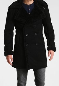 Manteau noir à double boutonnage avec grand col bordé de fourrure, boutons décoratifs et manches texturées. Confectionné en tissu doux avec une finition chaude.
