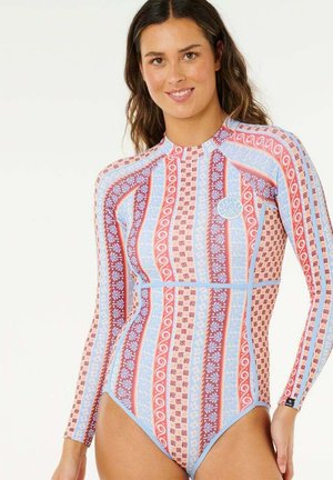 Mujer sonriente que lleva un traje de baño de una pieza con mangas largas, con rayas verticales en rojo, azul y beige, y diseños florales.