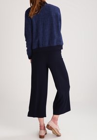 Navyblau strukturierte Jacke mit cropped Schnitt, kombiniert mit weit geschnittenen navyblauen Hosen. Helle rosa Socken und Schuhe mit Blockabsatz runden den Look ab.