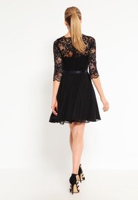 Svart klänning med bodice av spets med långa ärmar, en utställd kjol och ett midjeband i satin. Tyget är lätt och fluffigt. Klassisk design.