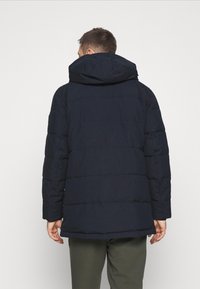 Marinblå pufferjacka med huva, kviltad textur, långa ärmar och rak passform. Har elastiska manschetter och en dold dragkedja.