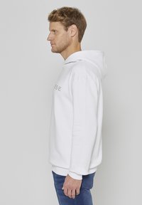 Sweat à capuche blanc à coupe décontractée, doté d'un logo frontal en gris doux. Texture de tissu douce, manches longues et poche kangourou à l'avant.