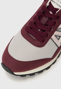 Chaussure de sport bordeaux et grise avec une tige en mesh, des accents en suède, des lacets plats et une semelle en caoutchouc. Présente un logo sur le côté et des détails texturés.