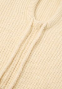 Maglione a maglia color crema con una texture a coste, dotato di un collo rotondo e di un dettaglio aperto nella parte anteriore. Materiale morbido e caldo.