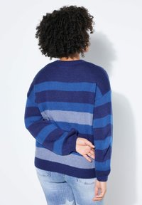 Blauer und marineblauer gestreifter Pullover mit lockerem Schnitt. Strickstruktur, Rundhalsausschnitt und überschnittene Schultern. Kombiniert mit ausgewaschenen blauen Jeans.