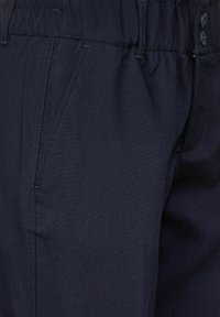 Marinblå byxor i mjukt tyg, med en avslappnad midja, sidofickor och subtila sömnadsdetaljer.