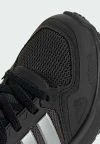 Chaussure de sport noire avec tige en mesh, accents en daim texturé et rayures argentées. Comprend un col rembourré et une semelle en caoutchouc durable.