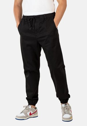 Pantalones jogger de algodón negro con una cintura elástica y cordón. Puños en los tobillos, con bolsillos laterales y una textura suave.