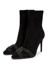 Bottes ankle en suede noir avec un bout pointu, un talon haut et un détail de sangle métallique nouée à l'avant. Texture lisse.
