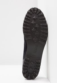 Semelle de botte en caoutchouc noir avec des crampons profonds et des motifs en forme de croix, affichant le nom de la marque "Gabor" embossé près du centre.