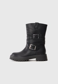 Mustad mustad nahast ankle boots on ümmarguse varbaga, paksu kummitallaga, millel on mustrid, ning kaks hõbedast klambrit, mis on paigaldatud jala keskele.