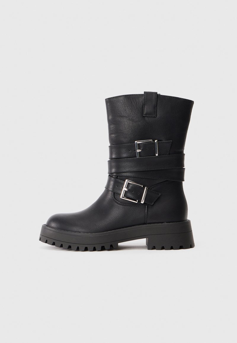Mustad mustad nahast ankle boots on ümmarguse varbaga, paksu kummitallaga, millel on mustrid, ning kaks hõbedast klambrit, mis on paigaldatud jala keskele.