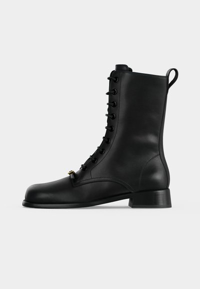 Bottine noire en cuir à lacets avec un talon bas et une languette à l'arrière, vue de côté extérieur sur un fond uni.