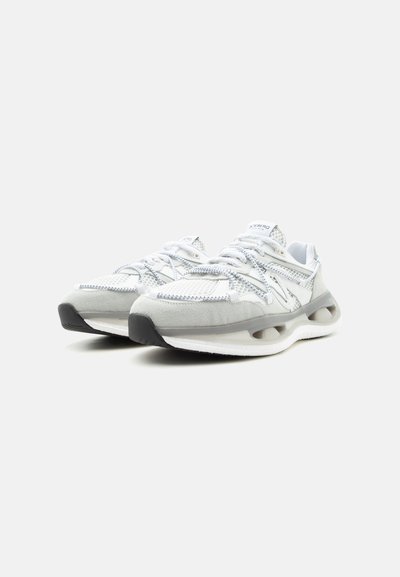 Ζευγάρι λευκά και γκρι αθλητικά παπούτσια με διχτυωτό υλικό, σουέντ λεπτομέρειες, παχύ σόλα με κοψίματα και κορδόνια σε απλό φόντο.